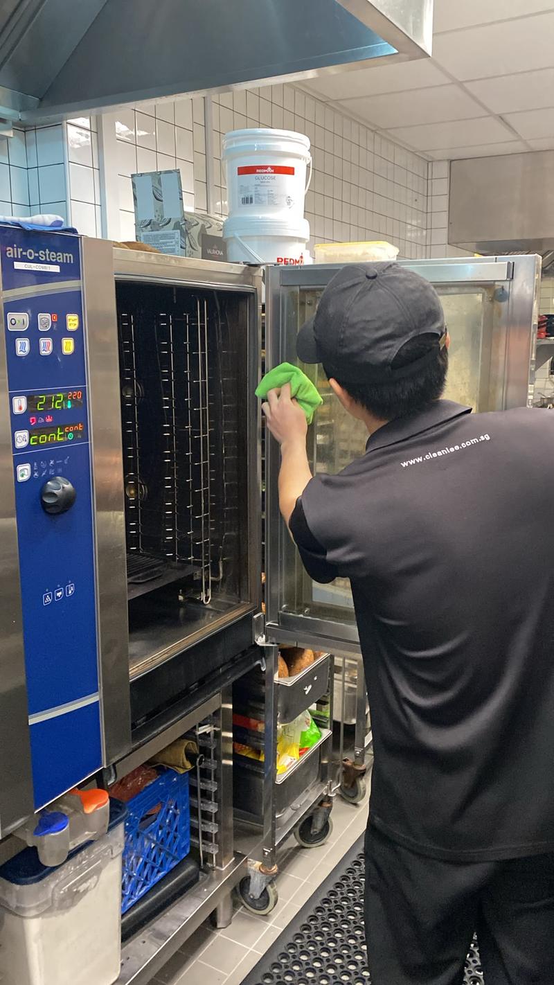 CleanLee staff in a branded uniform cleaning a combi steam oven in a commercial kitchen