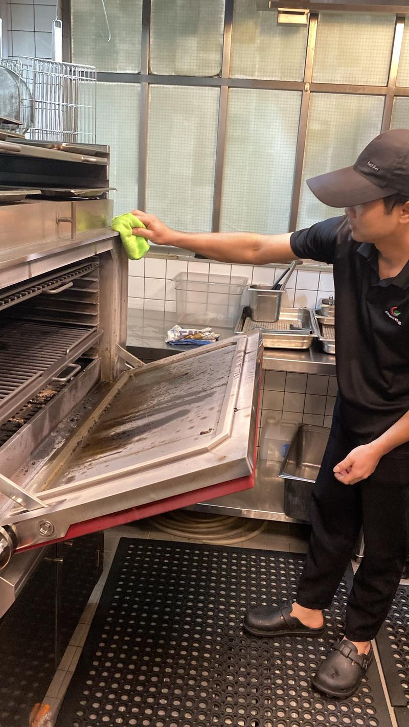 CleanLee staff wiping down the open door of a commercial oven in a restaurant kitchen