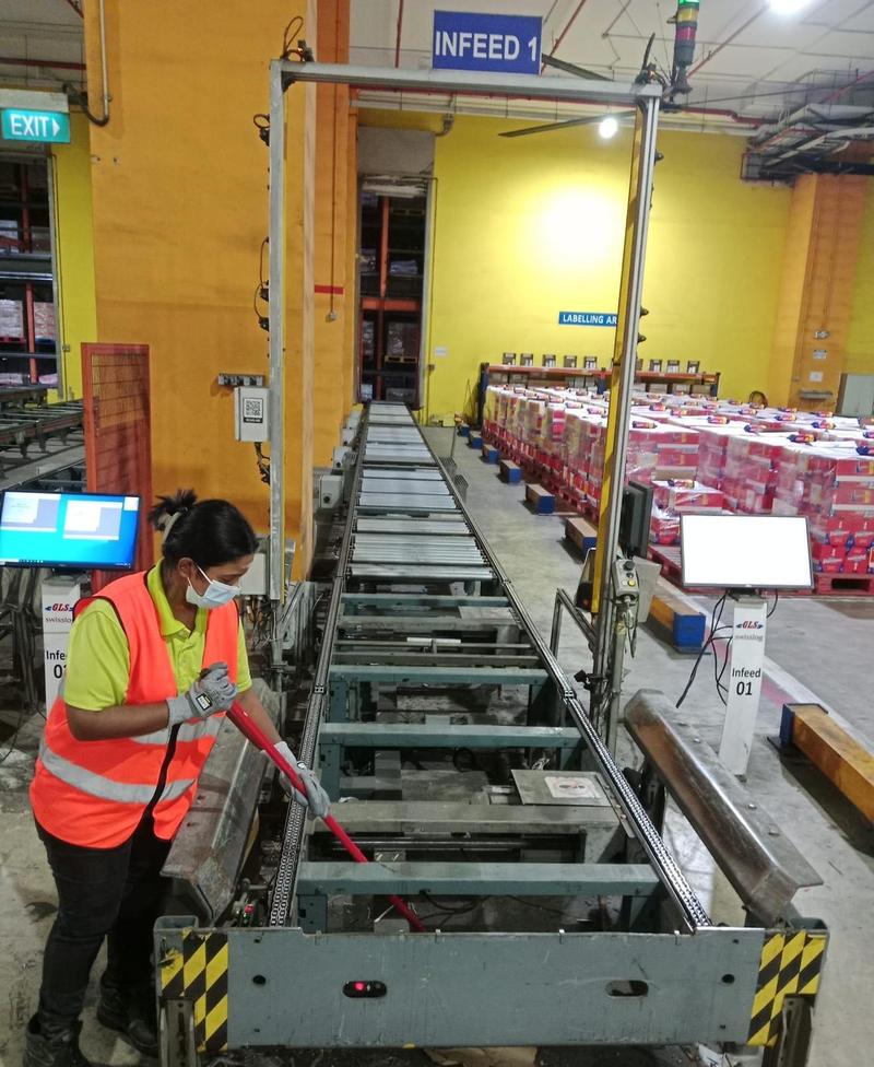 CleanLee cleaner brushing debris from a conveyor infeed line in a warehouse