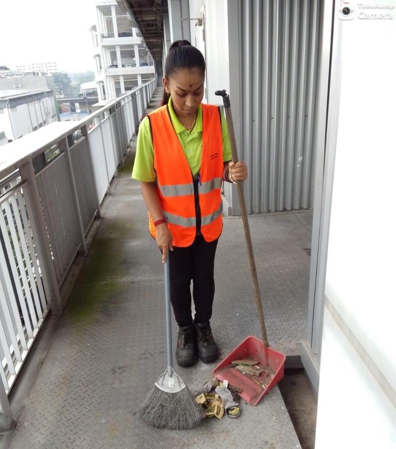 Cleaner in a hi-vis vest sweeping an external corridor of a commercial building