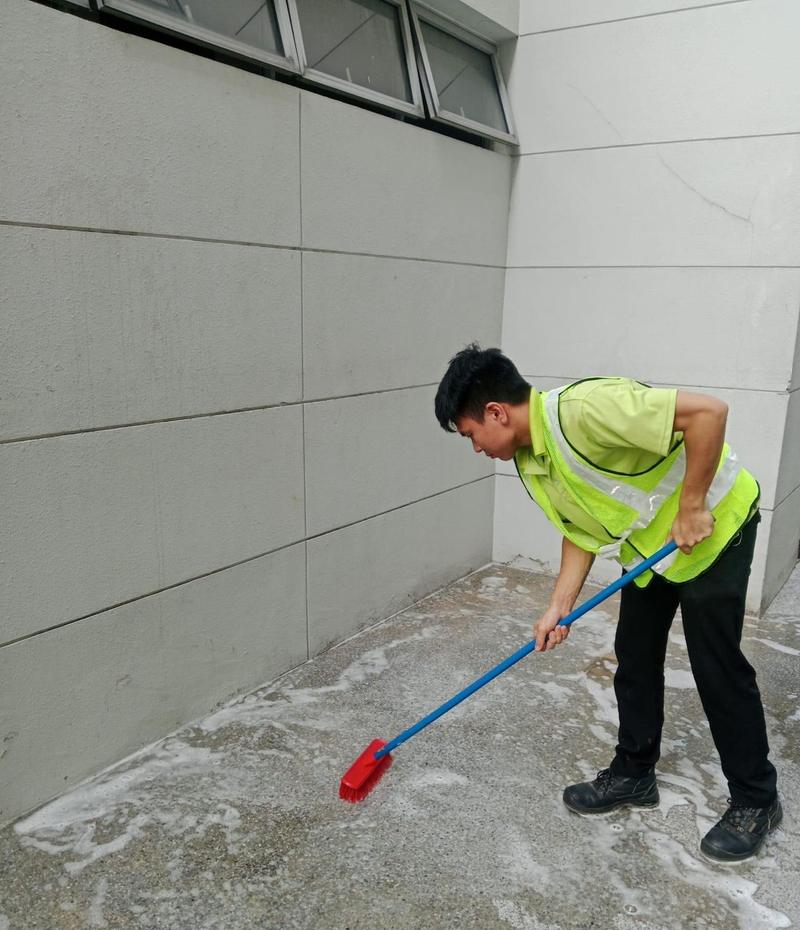 Cleaner scrubbing a soapy floor along a building wall with a deck brush
