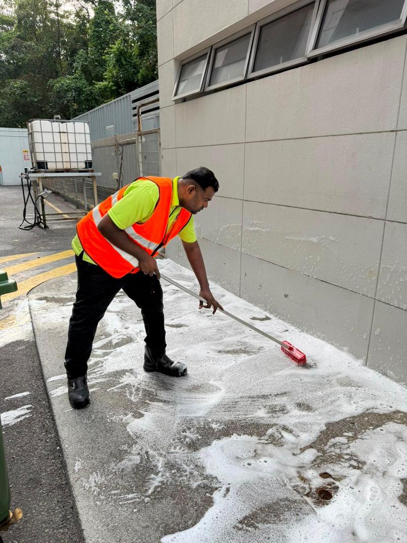 Cleaner scrubbing an external floor with detergent and a deck brush