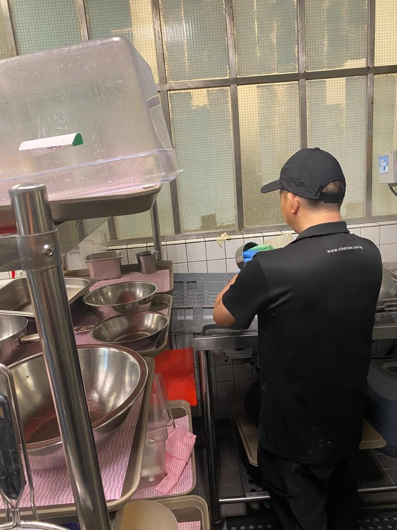 Kitchen helper organising mixing bowls and kitchenware at a restaurant prep area