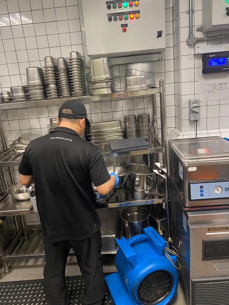 Kitchen helper working at pot and pan shelving while an air mover dries the kitchen floor
