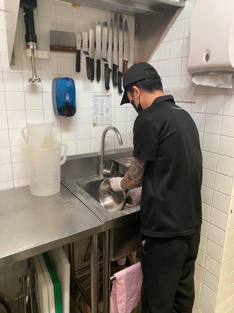 CleanLee kitchen helper washing utensils at a stainless steel prep sink in a commercial kitchen