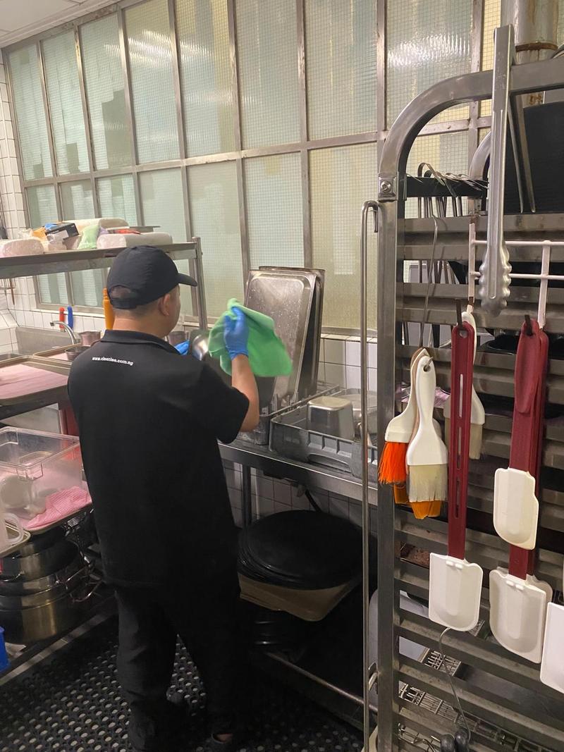 CleanLee kitchen helper wiping down a stainless steel workstation with a microfibre cloth