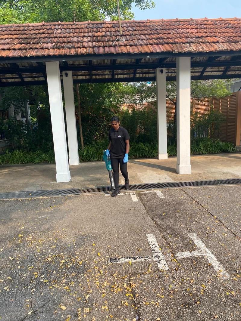 Cleaner sweeping leaves from an outdoor car park beside a sheltered walkway