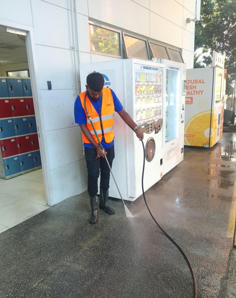 Cleaner pressure-washing a floor beside lockers and vending machines