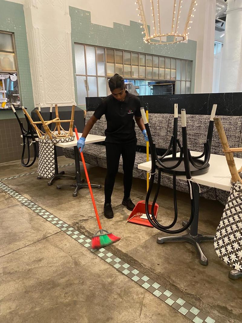 CleanLee cleaner sweeping a restaurant dining area with chairs stacked on tables