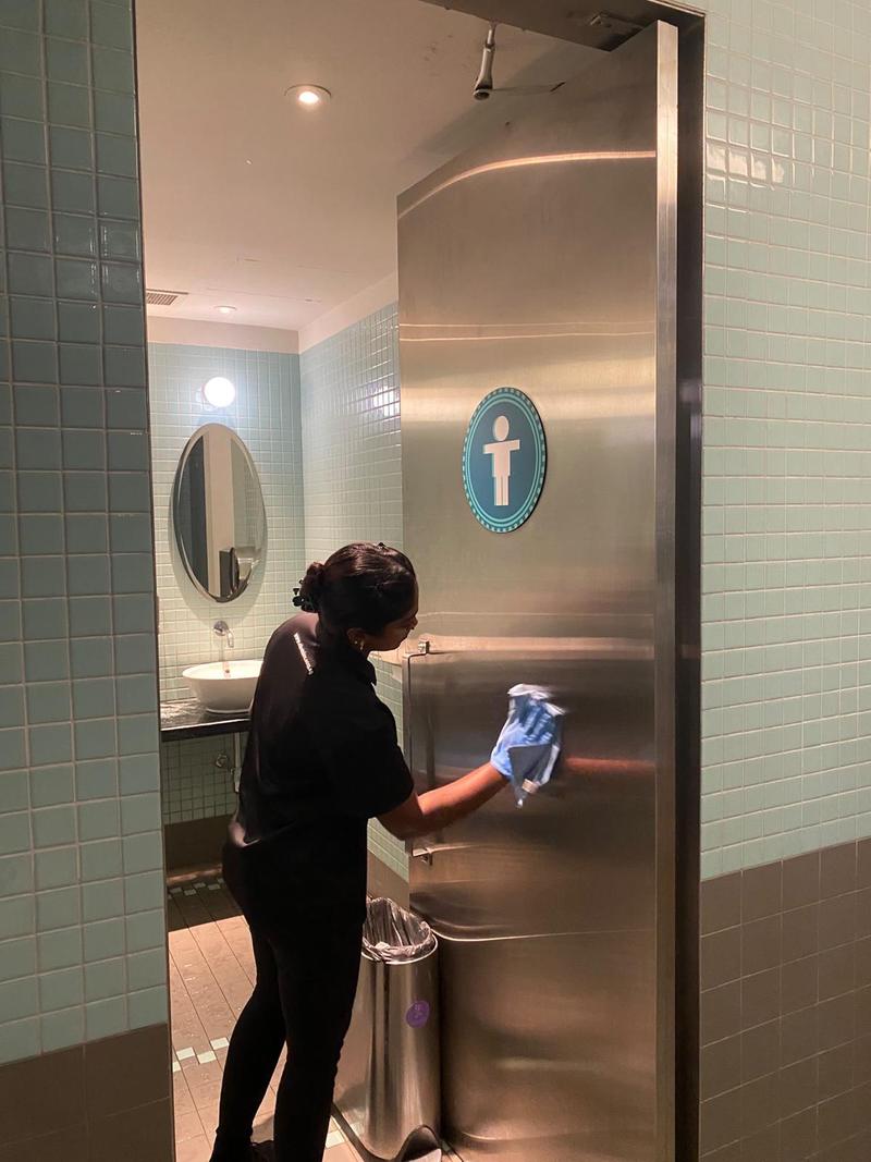 Cleaner sanitising a stainless steel washroom door and its handle