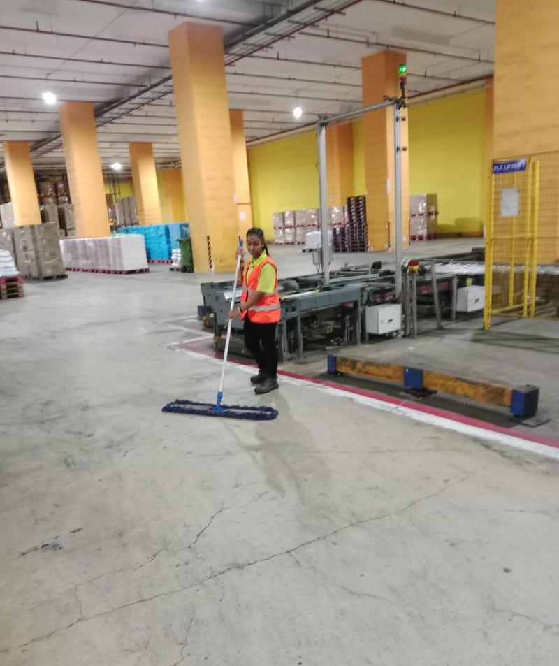 Cleaner dust-mopping a large warehouse floor near a loading area