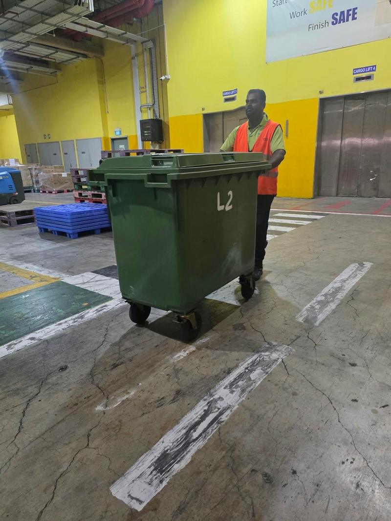 Cleaner in a hi-vis vest moving a large refuse bin across a warehouse floor