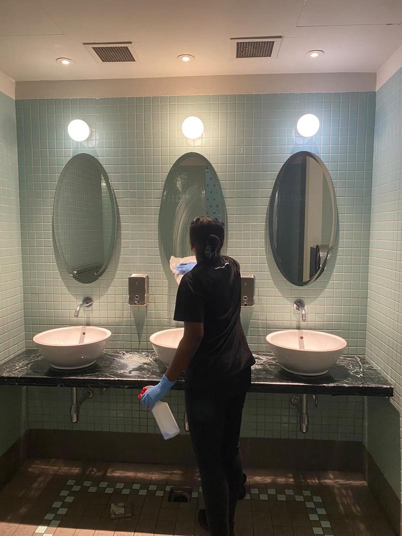 CleanLee cleaner spraying and wiping a washroom vanity with three basins and oval mirrors